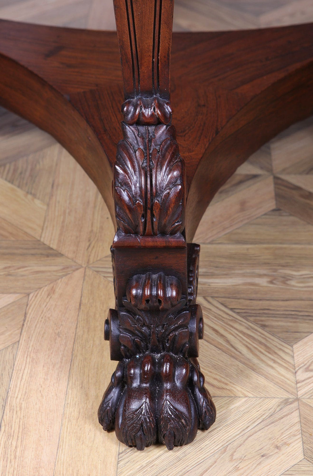Close-up of carved paw foot detail on the Regency Rosewood Drum Table wooden leg on parquet floor.