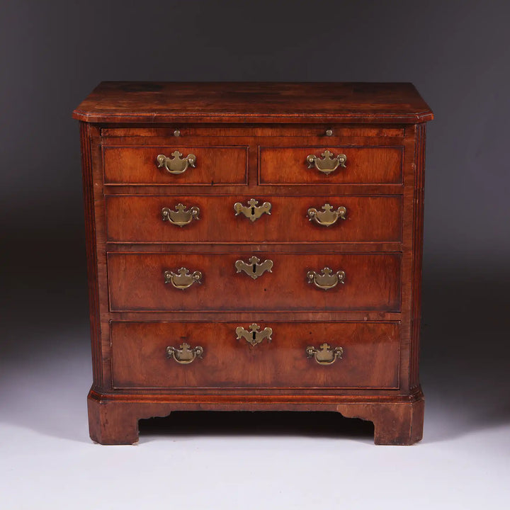George I Walnut Chest of Drawers with feather banding, five drawers, brass handles, canted corners, and bracket feet, circa 1715.