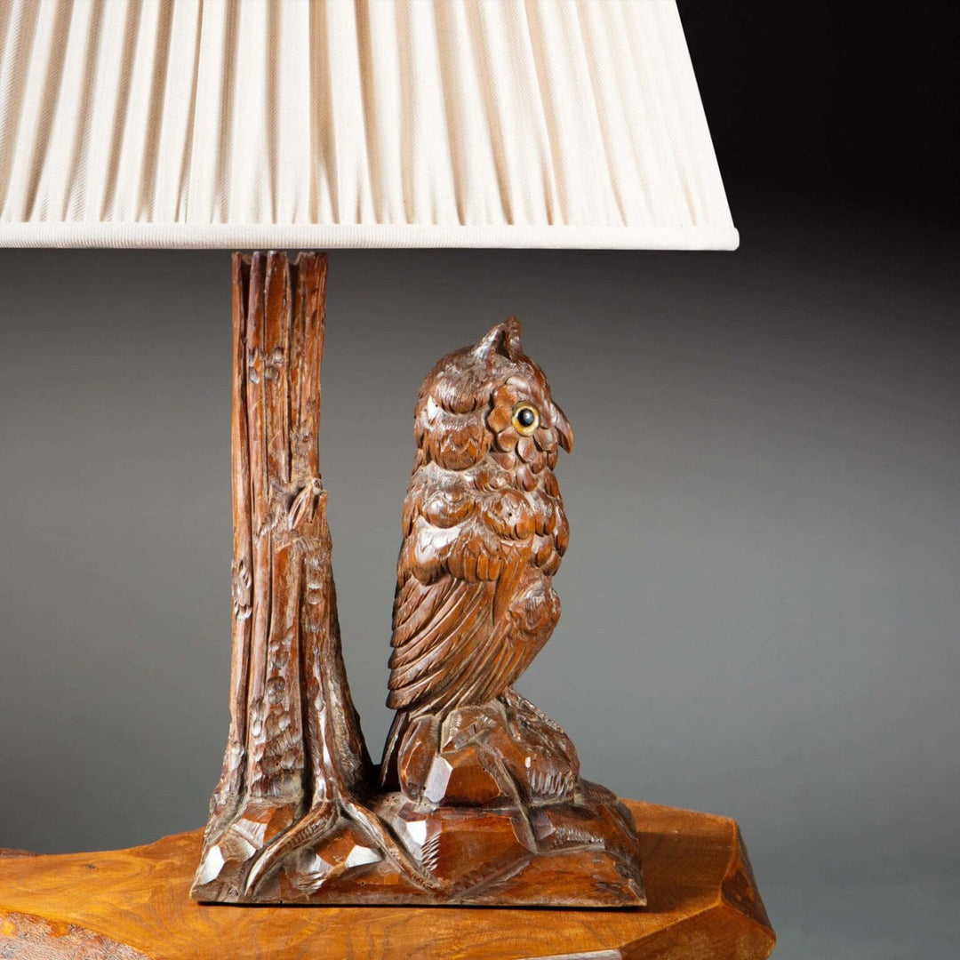 Carved Owl As A Table Lamp with detailed 19th century wooden owl figure and cream pleated lampshade on wooden table.
