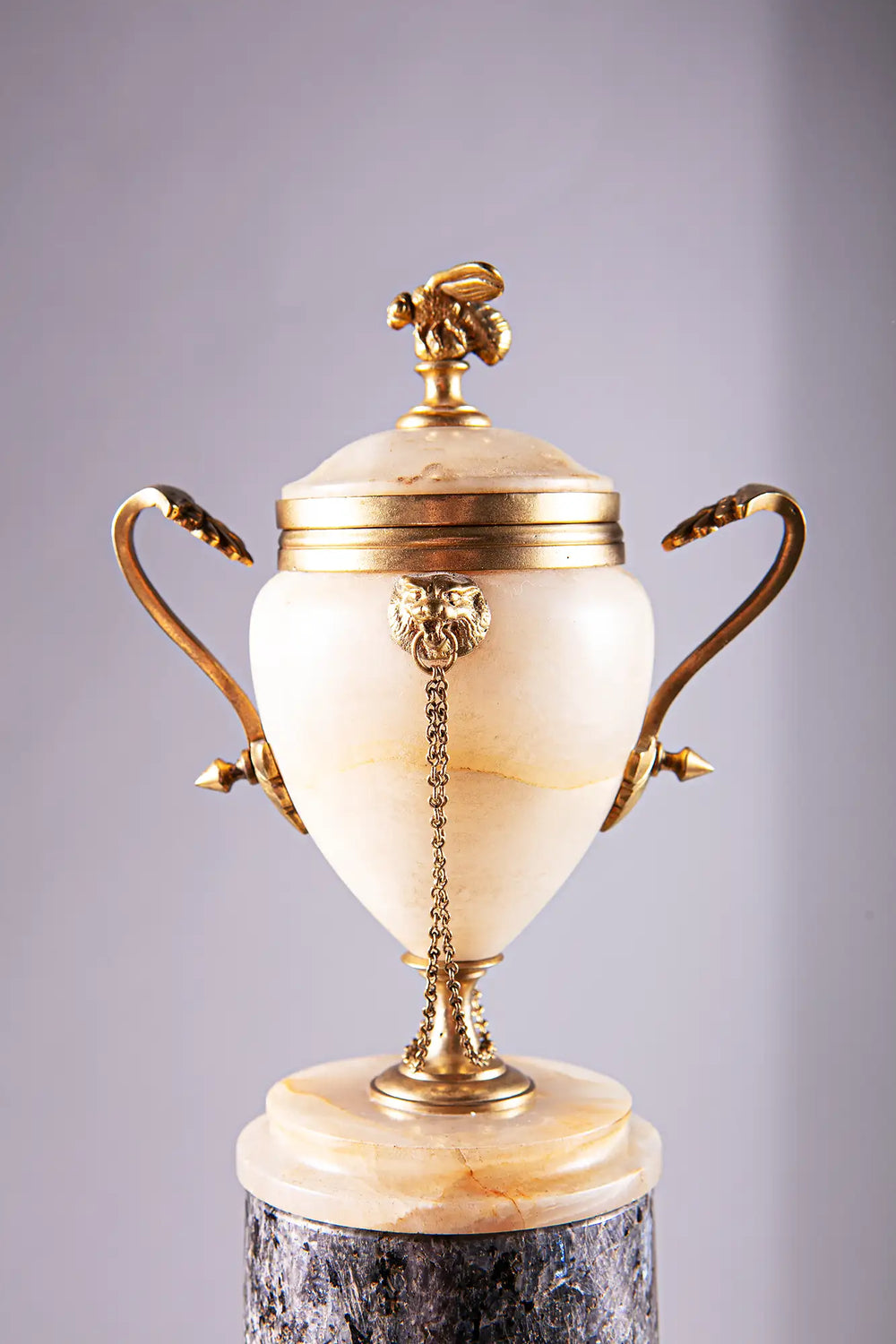 Neoclassical Urn on Granite Pedestal with polished alabaster, gilded bronze lion handles, bee finial, and chain details.