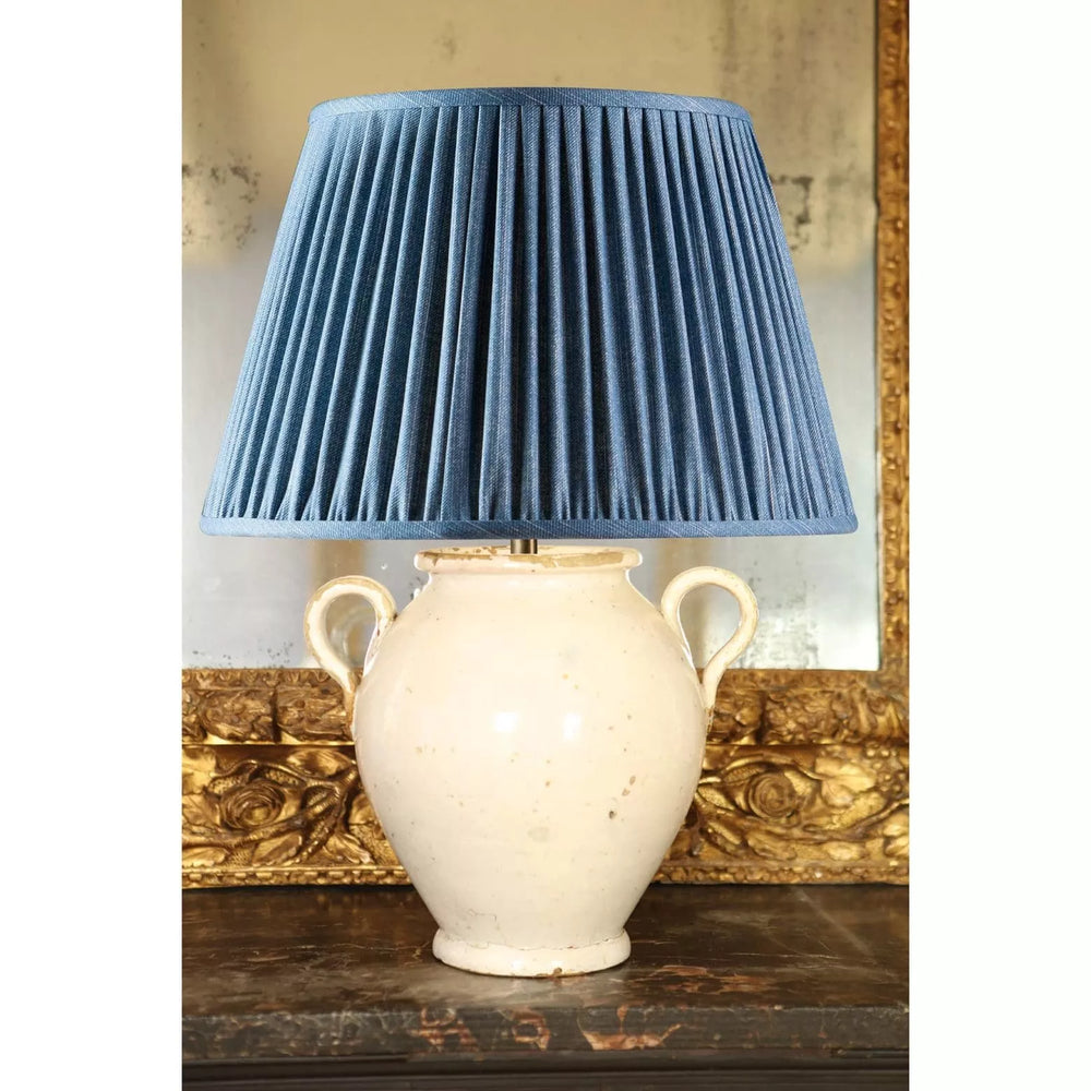 Italian 17th Century Vase Mounted as a Lamp with cream glaze and blue pleated lampshade on rustic wooden surface.