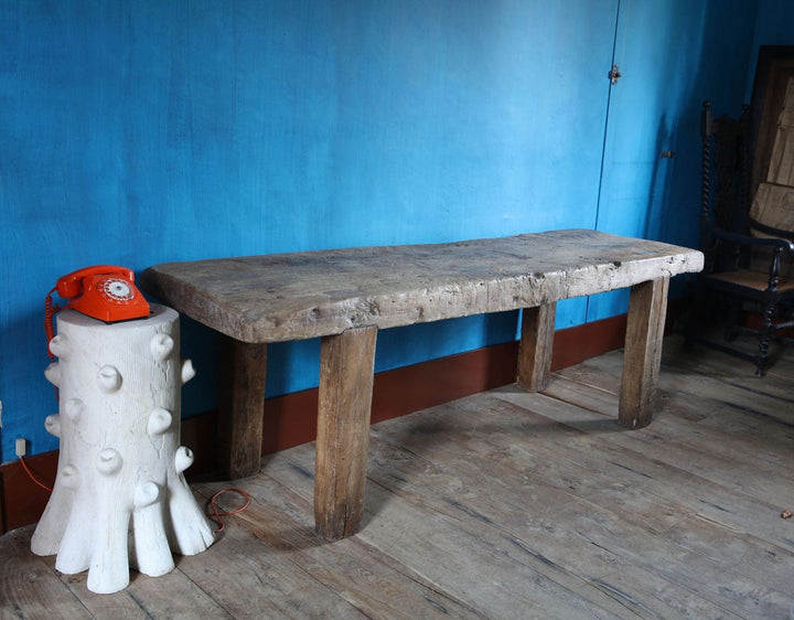 French 18th Century Rustic Farm Table made from worn elm wood with sturdy legs against a blue wall in a vintage room.