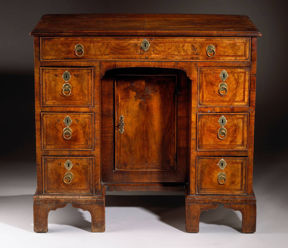George I Walnut Kneehole Desk with feather banding, brass handles, cupboard, and drawers on ogee bracket feet.
