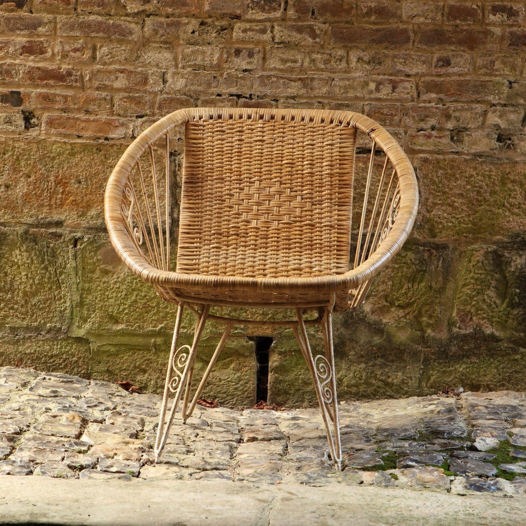 Modernist wireframe rattan chair from Collection EE30 with woven seat and slender metal frame against rustic wall