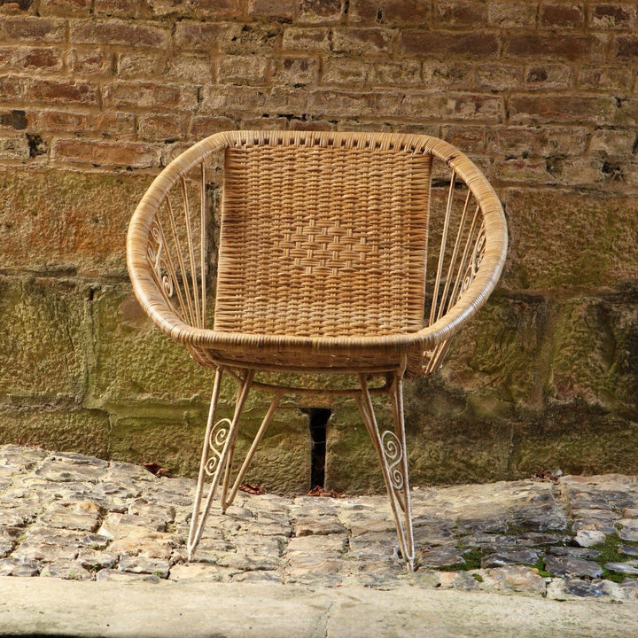 Modernist wireframe rattan chair from Collection EE30 with woven seat and slender metal frame against rustic wall