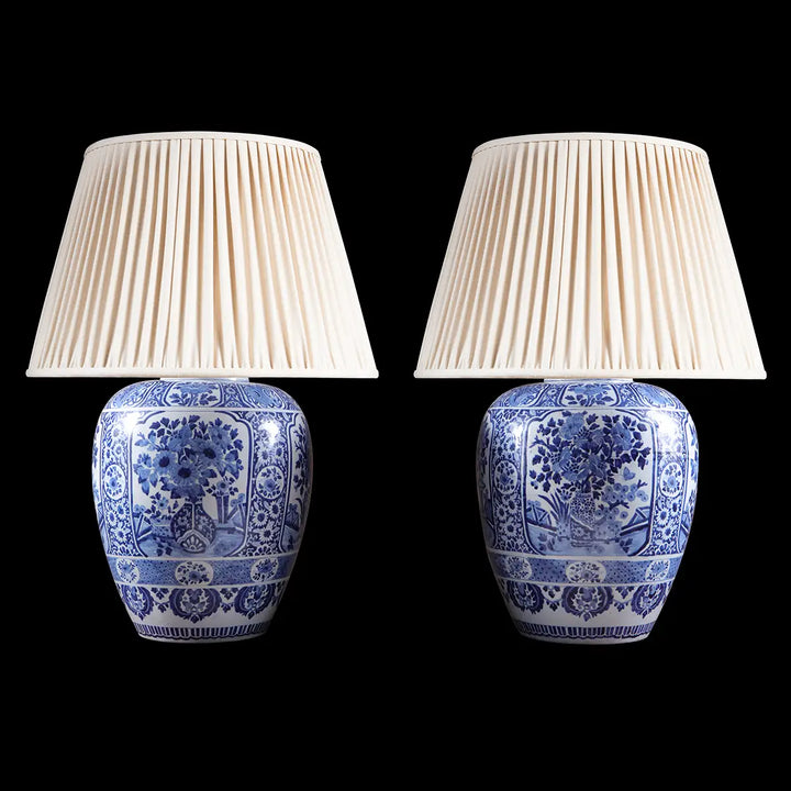 Large Pair of Blue and White Delft Table Lamps with traditional floral patterns and pleated beige shades on black background.