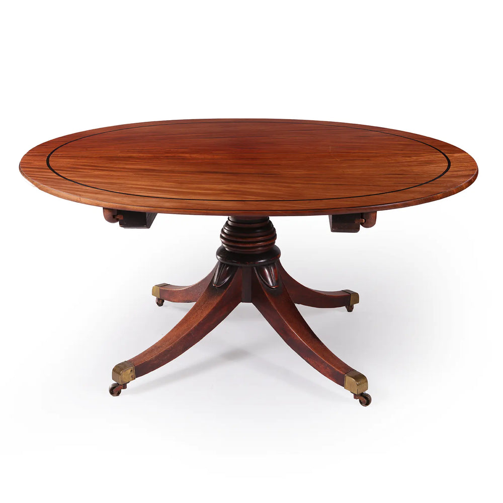 Extending Oval Dining Table in the Manner of George Bullock, mahogany oval top with pedestal base and cast brass castors.