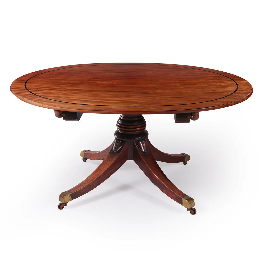 Extending Oval Dining Table in the Manner of George Bullock, mahogany oval top with pedestal base and cast brass castors.