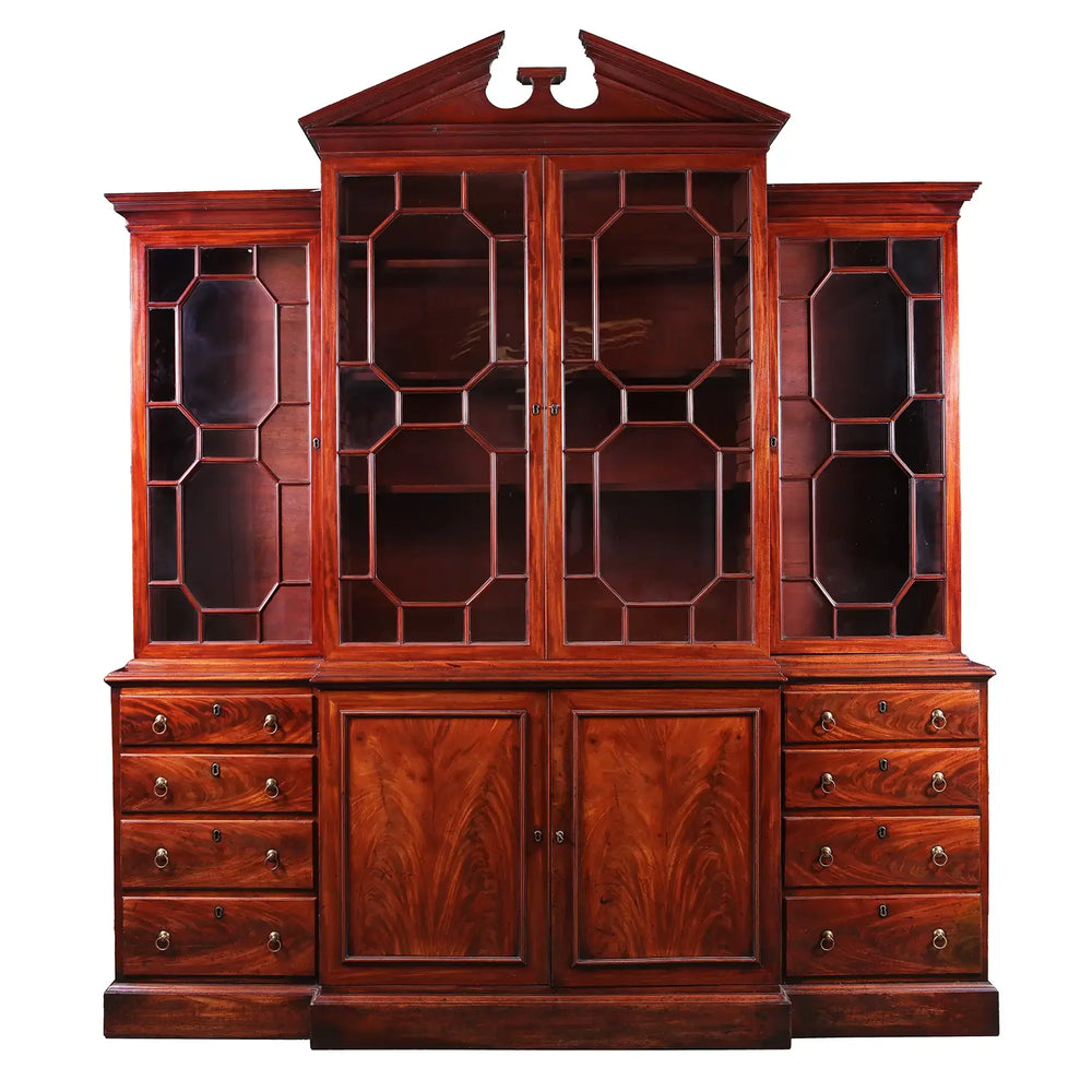 GEORGE III MAHOGANY BREAKFRONT BOOKCASE with glazed astragal doors, mahogany drawers, and broken pediment circa 1770.