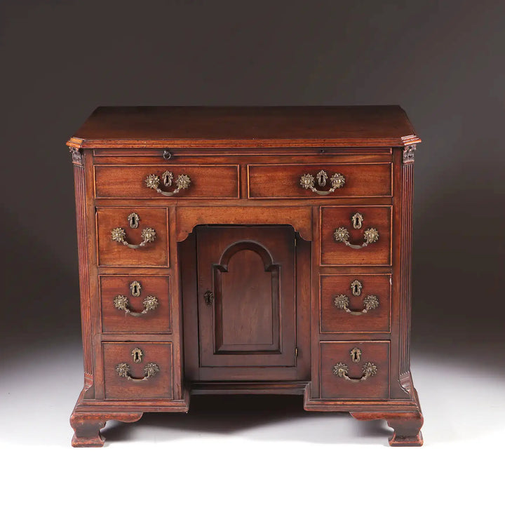 GEORGE II MAHOGANY KNEEHOLE DESK with brass handles, central cupboard, and ogee bracket feet, circa 1725 English antique.