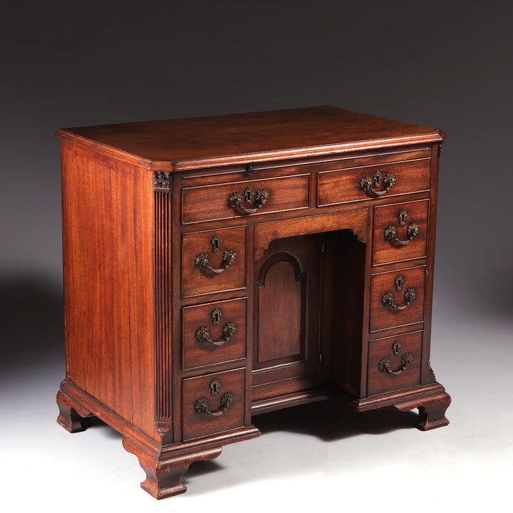 GEORGE II MAHOGANY KNEEHOLE DESK with brass handles, ogee bracket feet, and finely figured mahogany wood, circa 1725.