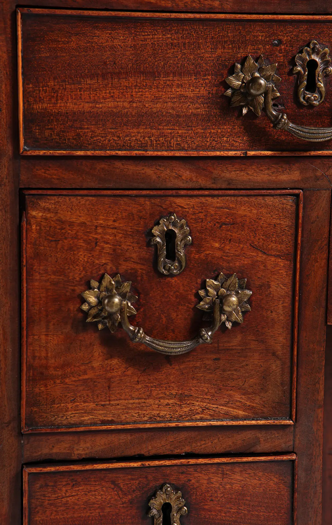 GEORGE II MAHOGANY KNEEHOLE DESK close-up of brass handles and keyhole on finely figured mahogany drawers.