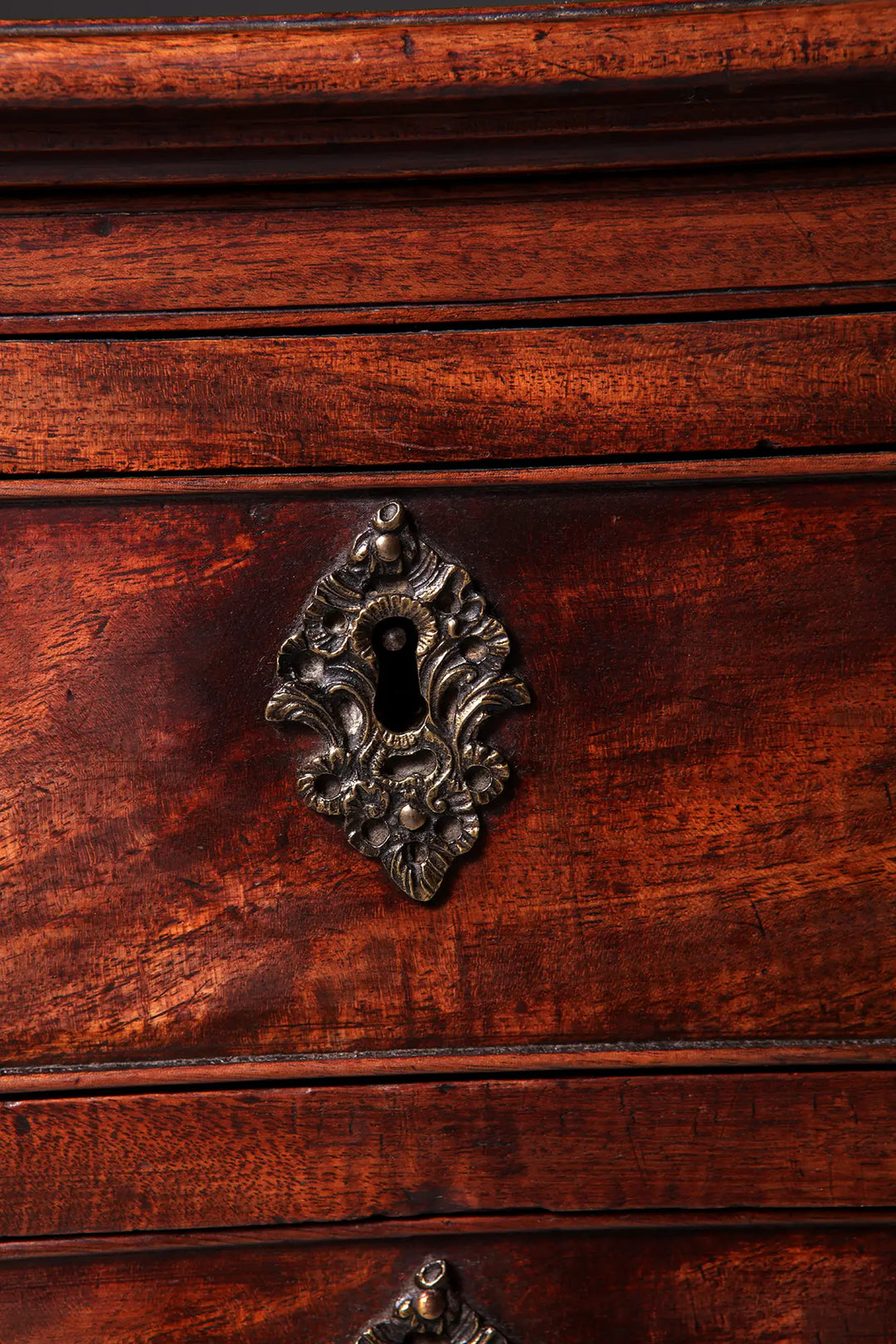 Close-up of ornate keyhole on GEORGE II MAHOGANY CHEST OF DRAWERS showing rich mahogany grain and patina.