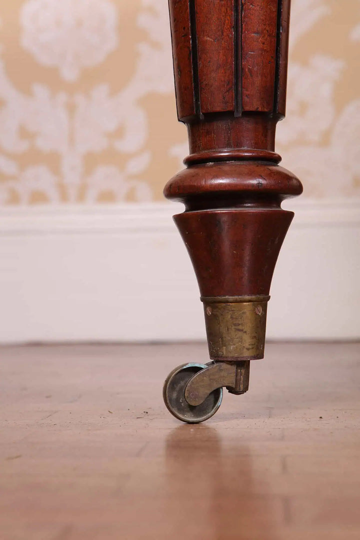 Regency Fiddleback Mahogany Partners Writing Table detailed carved leg with brass castor on wooden floor.