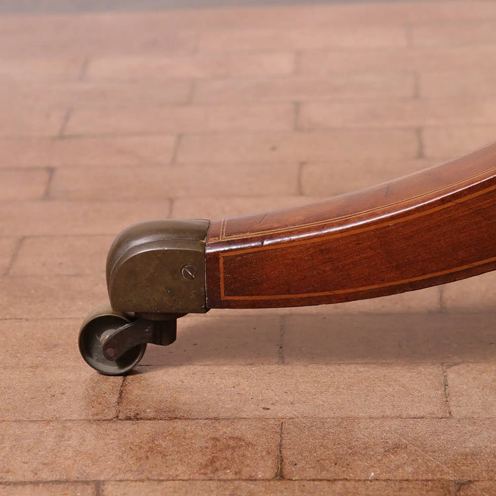Sheraton Mahogany Drum Table pedestal leg with brass castor on a tiled floor, showing wood grain and craftsmanship.
