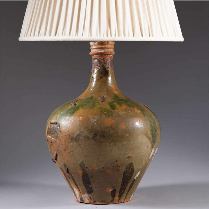 Glazed Ceramic Bottle Vase With Old Restorations Mounted as a Table Lamp with a cream fabric shade and antique finishes.