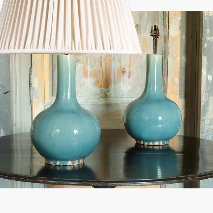 Pair of Blue Celadon Chinese Bottle Vase Lamps with smooth glaze finish on a dark wooden table against rustic background.