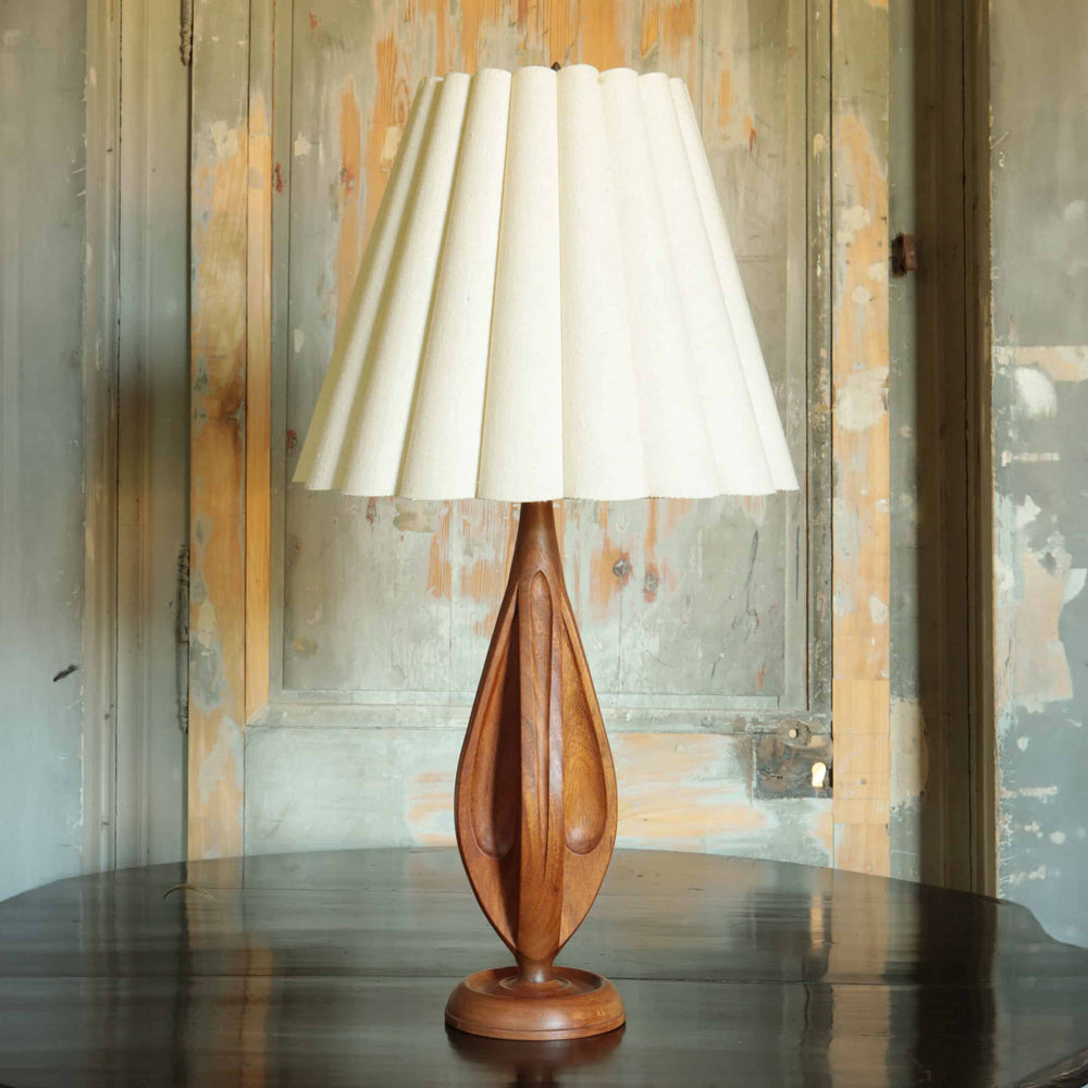 Mid Century Wooden Lamp and Shade with a sculpted wooden base and pleated white fabric shade on wooden table.