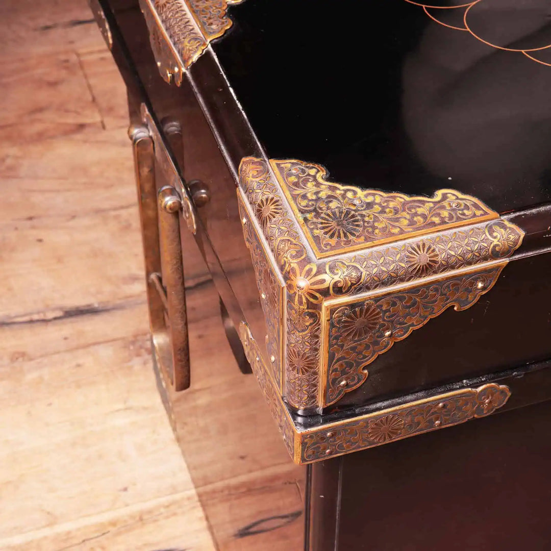 Edo Japanese Black Lacquer and Gilt Trunk showing detailed brass corner mounts and drop handles on wooden floor.