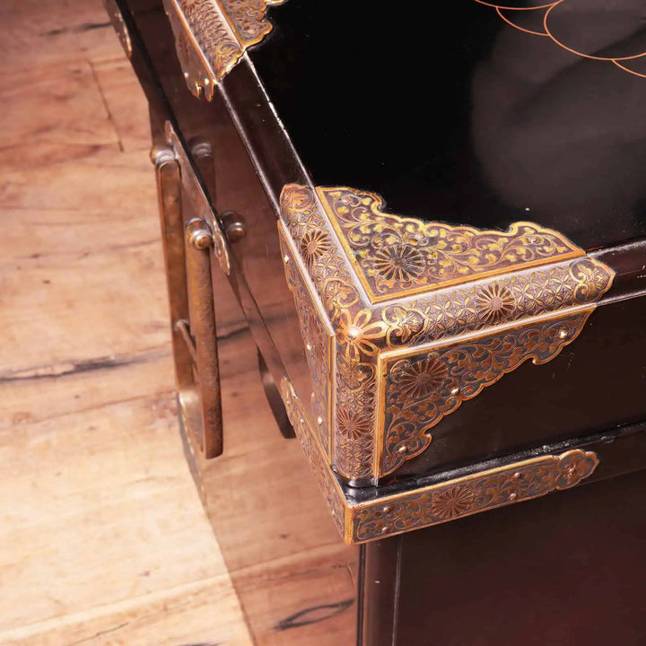 Edo Japanese Black Lacquer and Gilt Trunk showing detailed brass corner mounts and drop handles on wooden floor.