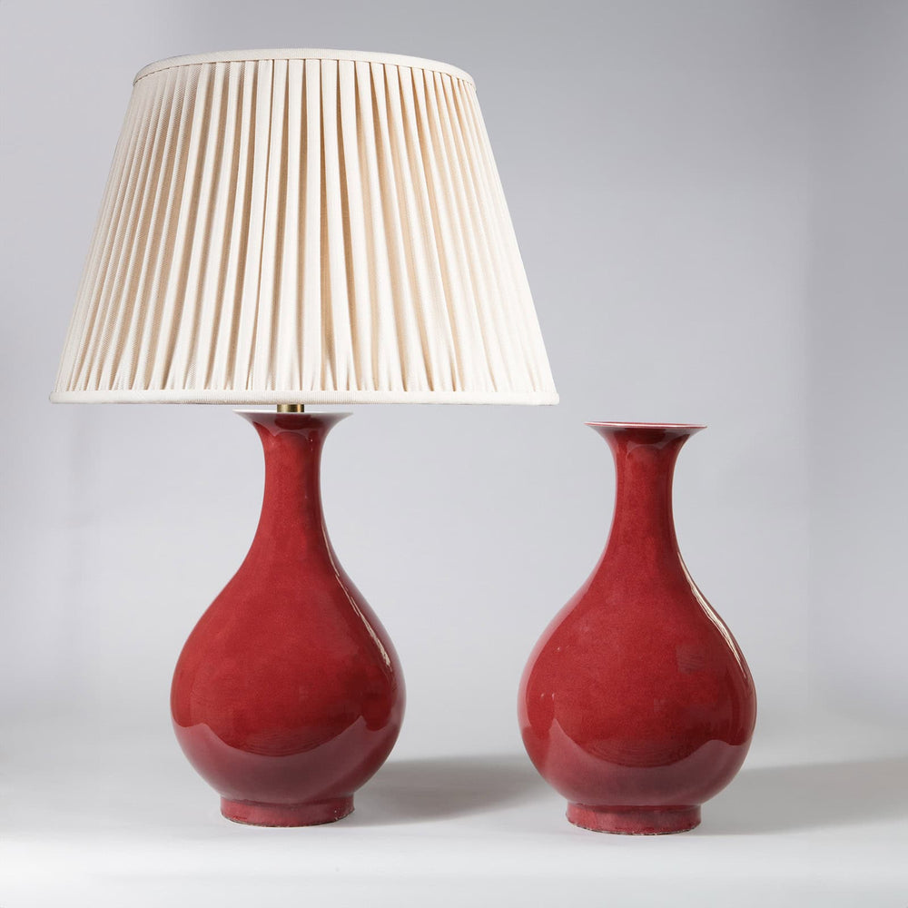 Pair of Meiping Sang de Boeuf Table Lamps with deep red porcelain glaze, one with cream pleated lampshade, one without.
