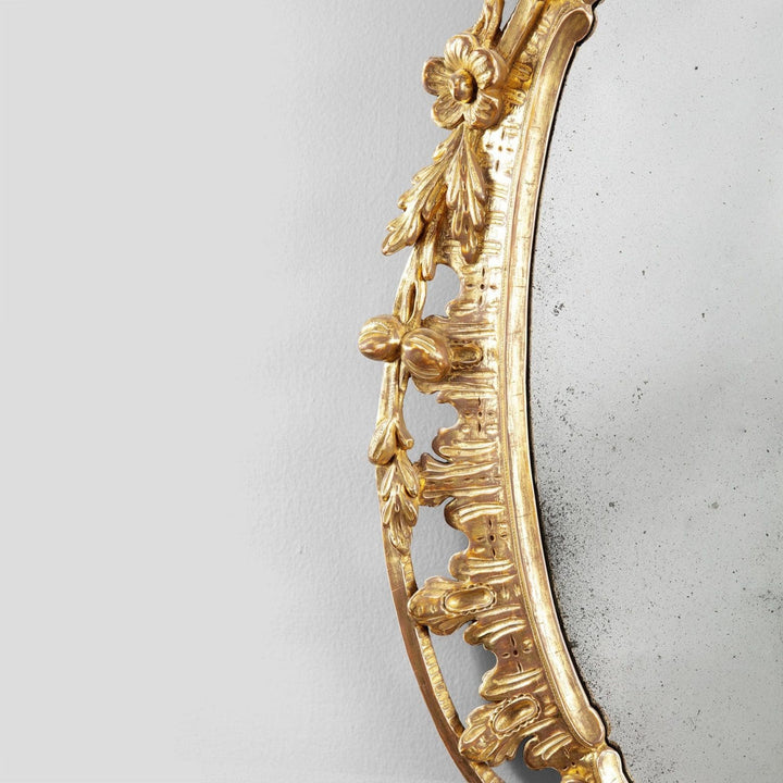 George III Rococo giltwood oval mirror with intricate C and S scrolls and floral swags from circa 1770 England.