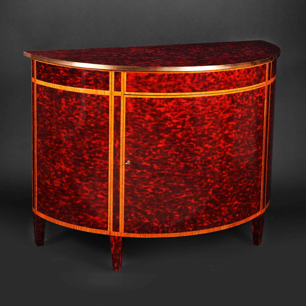 A Demi Lune tortoiseshell cabinet by Mallett with red simulated tortoiseshell and brass banded edge.
