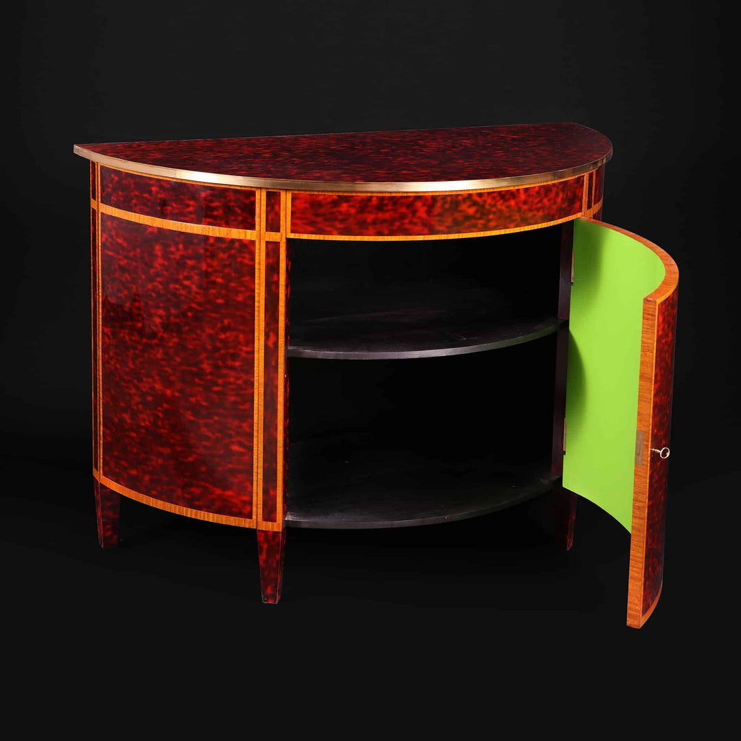 A Demi Lune tortoiseshell cabinet by Mallett with brass band, mahogany cross-banding, and bright green interior shelves.