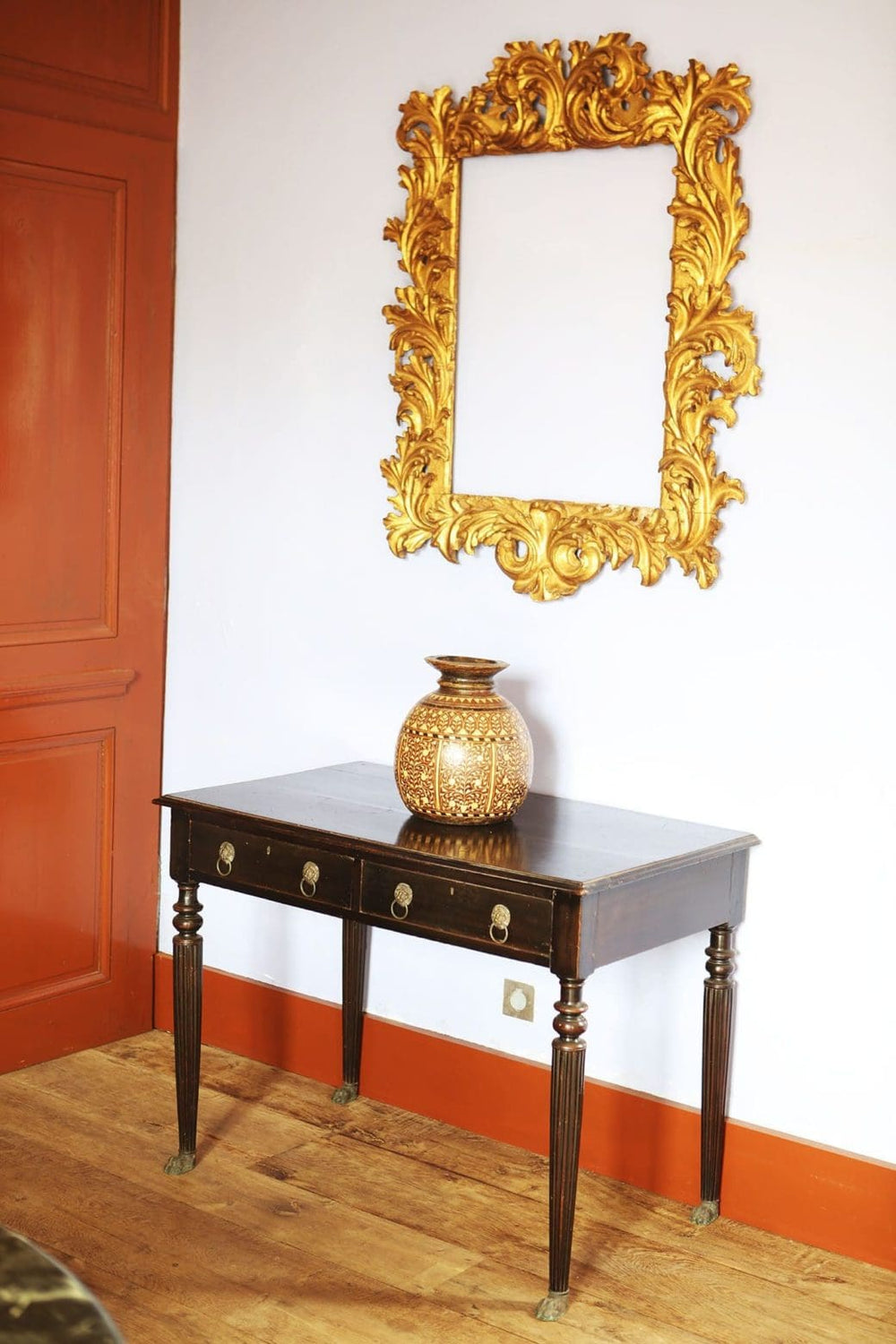 Anglo Indian Ebonised Writing Table with lion mask handles on fluted legs and brass paw feet in a room corner.