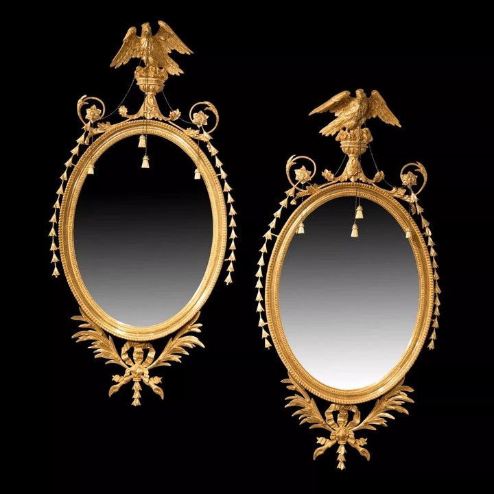 Pair of George III Giltwood Oval Mirrors with neoclassical eagles, tassels, and palm leaf decorations, circa 1770 England.