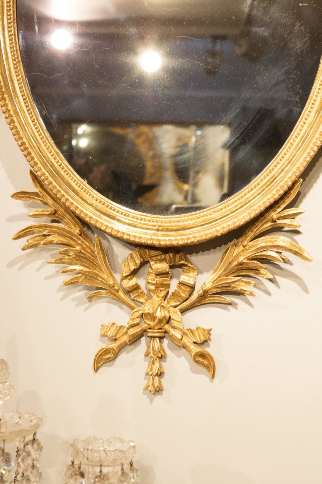 Pair of George III Giltwood Oval Mirrors with ornate palm leaf and bow designs, circa 1770, England, 109 cm high.