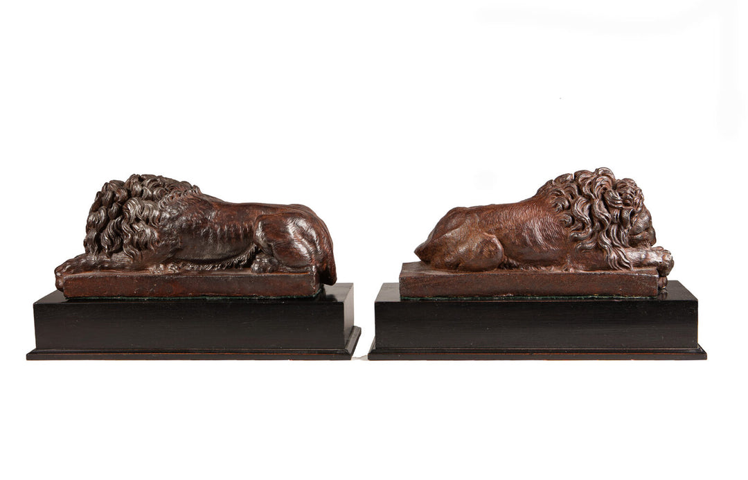 Pair of Cast Iron Versions of the Canova Lions showing detailed antique sculptures of sleeping and vigilant lions on black bases.