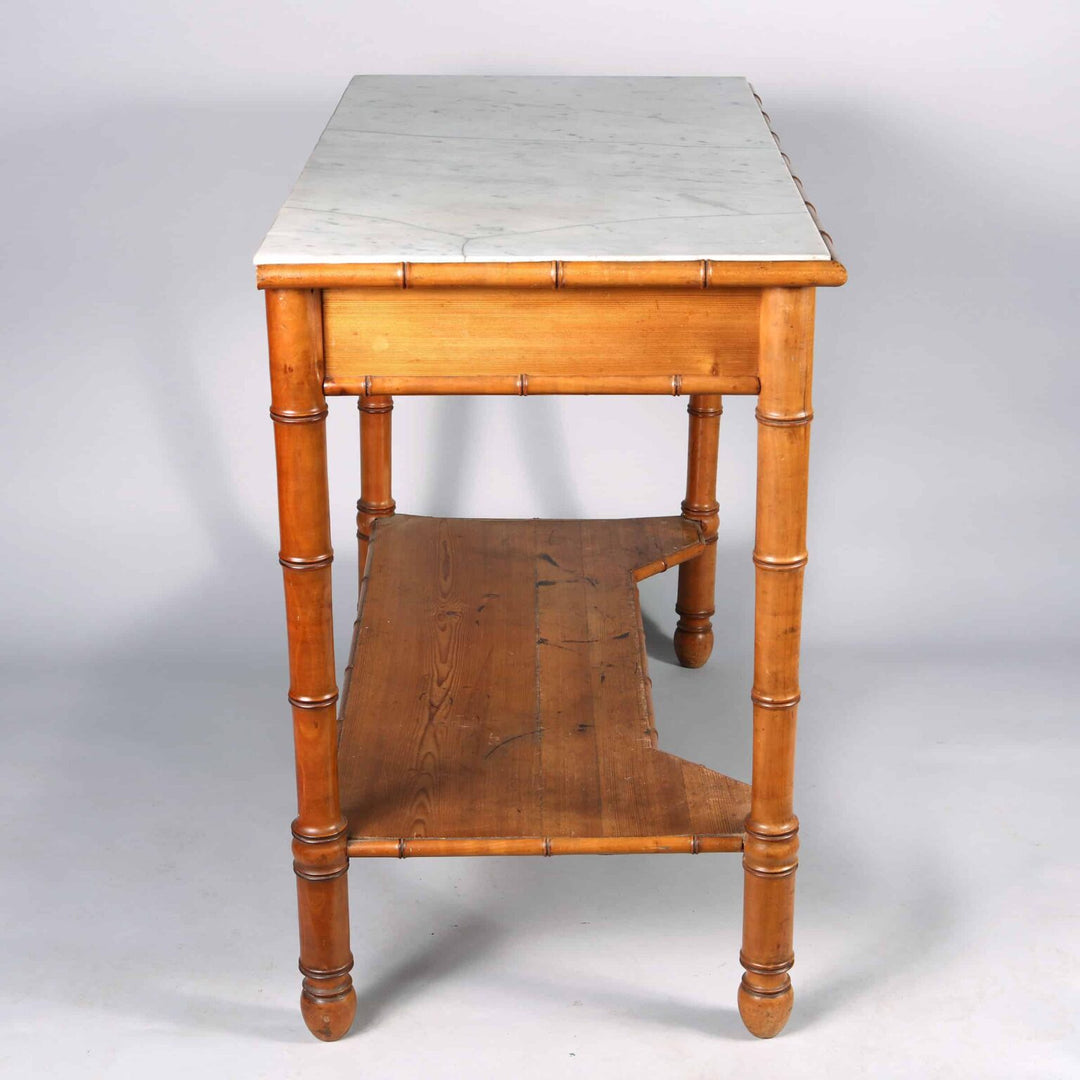 A Napoleon III simulated bamboo console desserte with white marble top, two drawers, and lower wooden tier.