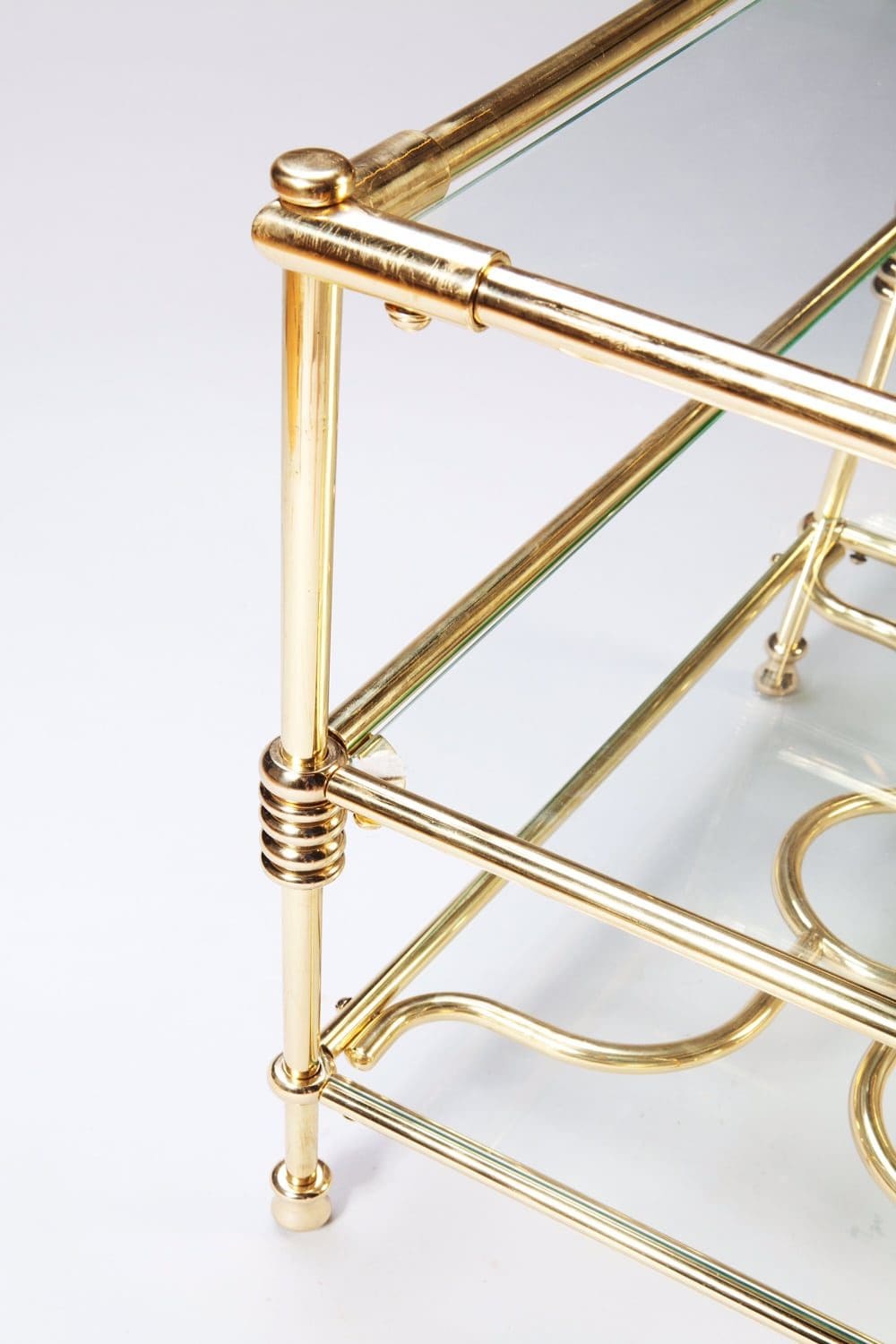 A close-up of the brass frame detailing on the Three Tiered Brass Art Deco Etagere with glass shelves.