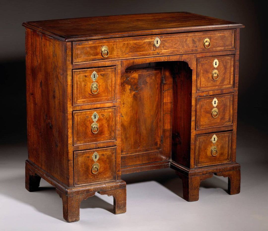 George I Walnut Kneehole Desk with brass ring handles, feather banding, and ogee bracket feet, circa 1715 England.