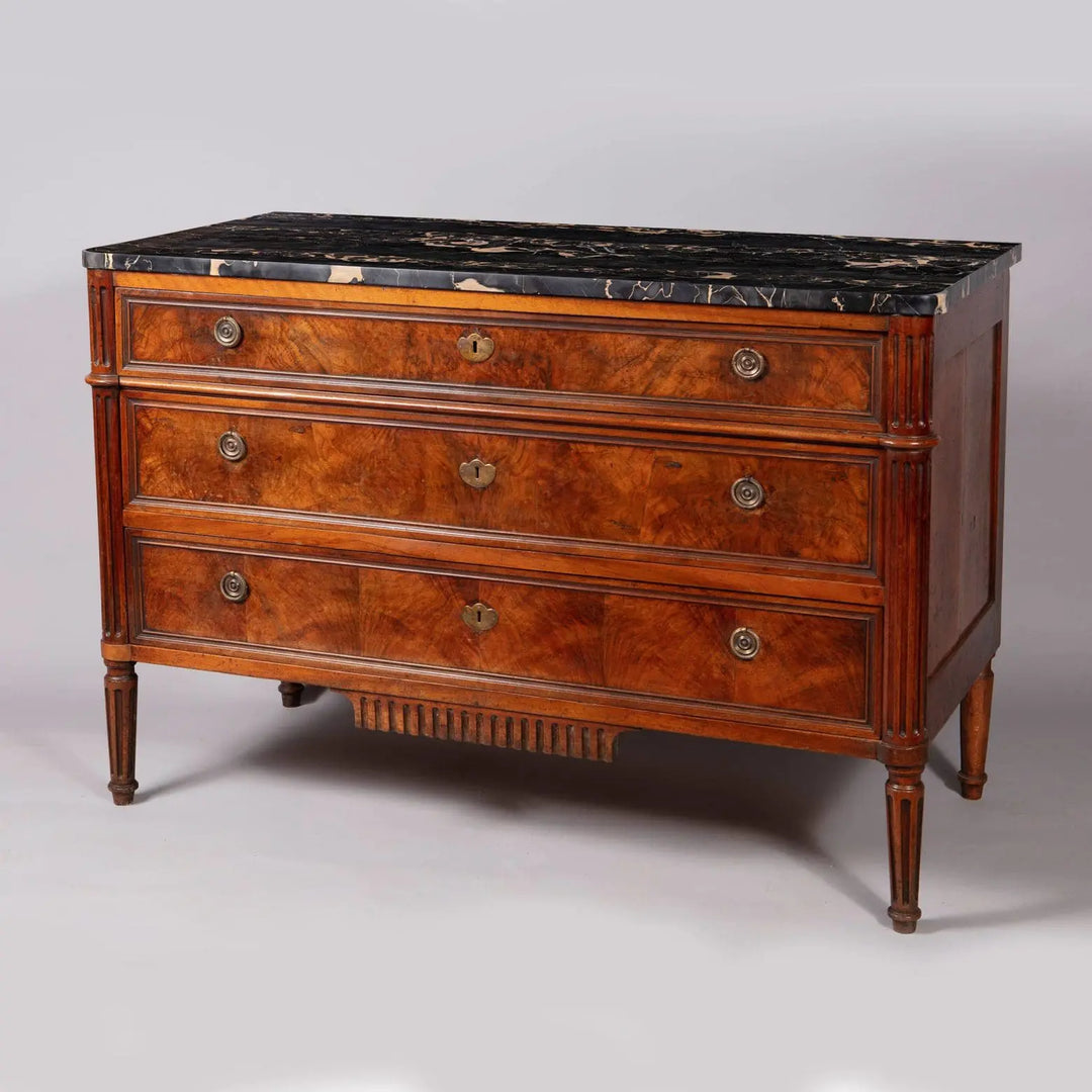 A French provincial Louis XVI commode with burr walnut veneer, Nero Portoro marble top, and fluted legs, stamped COURTE.