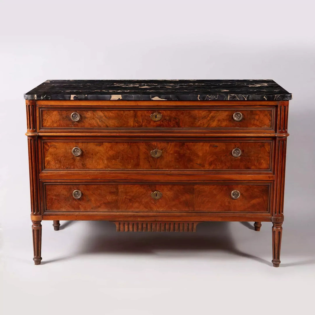 A French provincial Louis XVI commode with burr walnut veneer, Nero Portoro marble top, and fluted legs stamped COURTE.