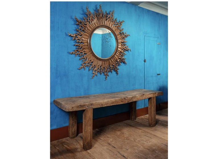 Zeus Mirror large round carved mirror with lightning bolts and antique finish hanging on blue wall above wooden bench