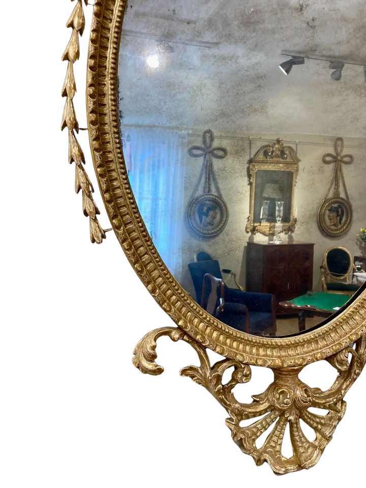 John Linnell Oval Gilt Mirror with intricate carved giltwood frame reflecting antique furnishings.