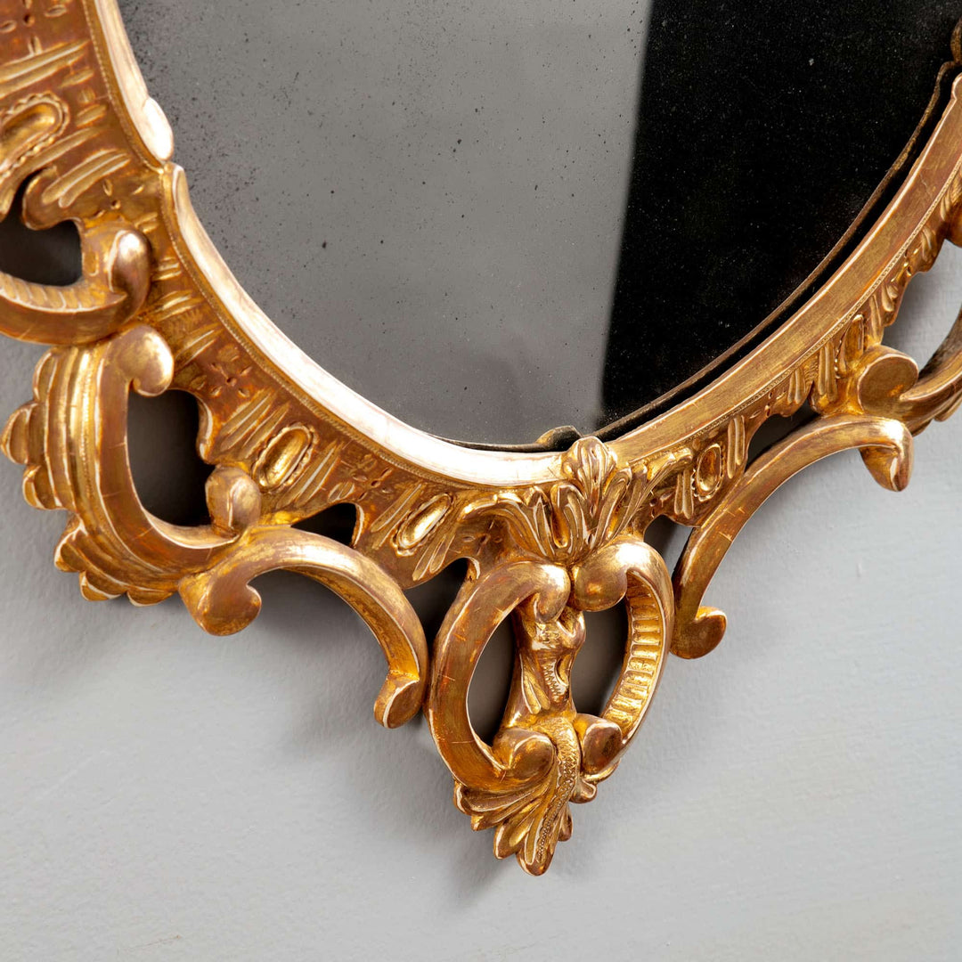 George III Rococo giltwood oval mirror with intricate scrolls and foliage detailing, circa 1770 England.