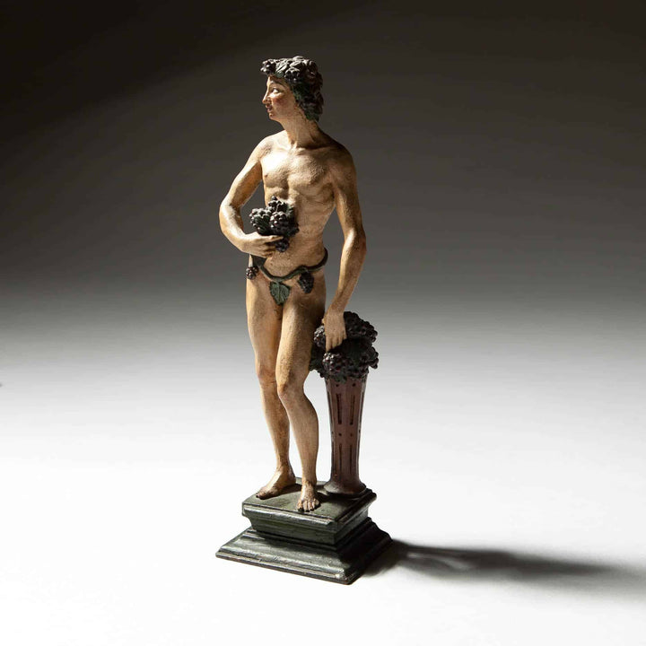 Flemish Carved Wooden Polychrome Figure Of Bacchus holding grapes standing on a plinth with vines in hair and clothing.