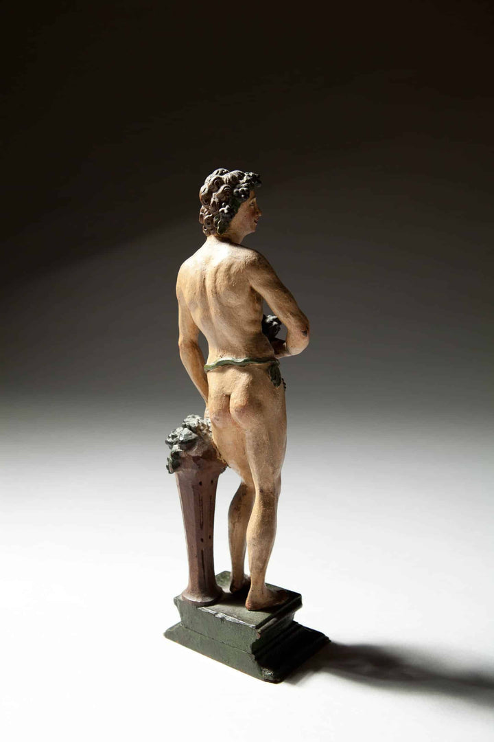 Flemish Carved Wooden Polychrome Figure Of Bacchus showing Bacchus holding grapes on a stepped plinth with vines.