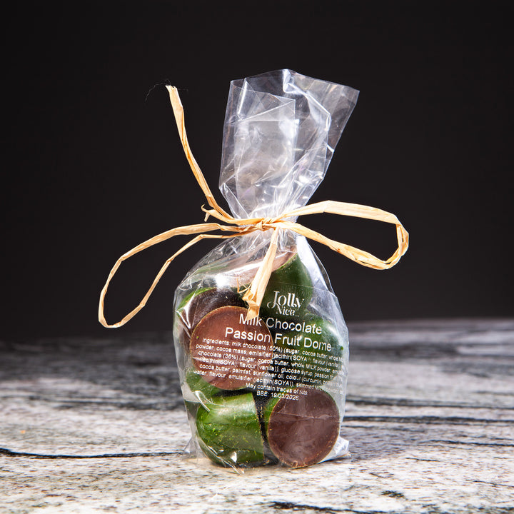 Clear bag of Jolly Nice milk chocolate passion fruit domes tied with raffia on rustic stone surface by Nicholas Wells Antiques